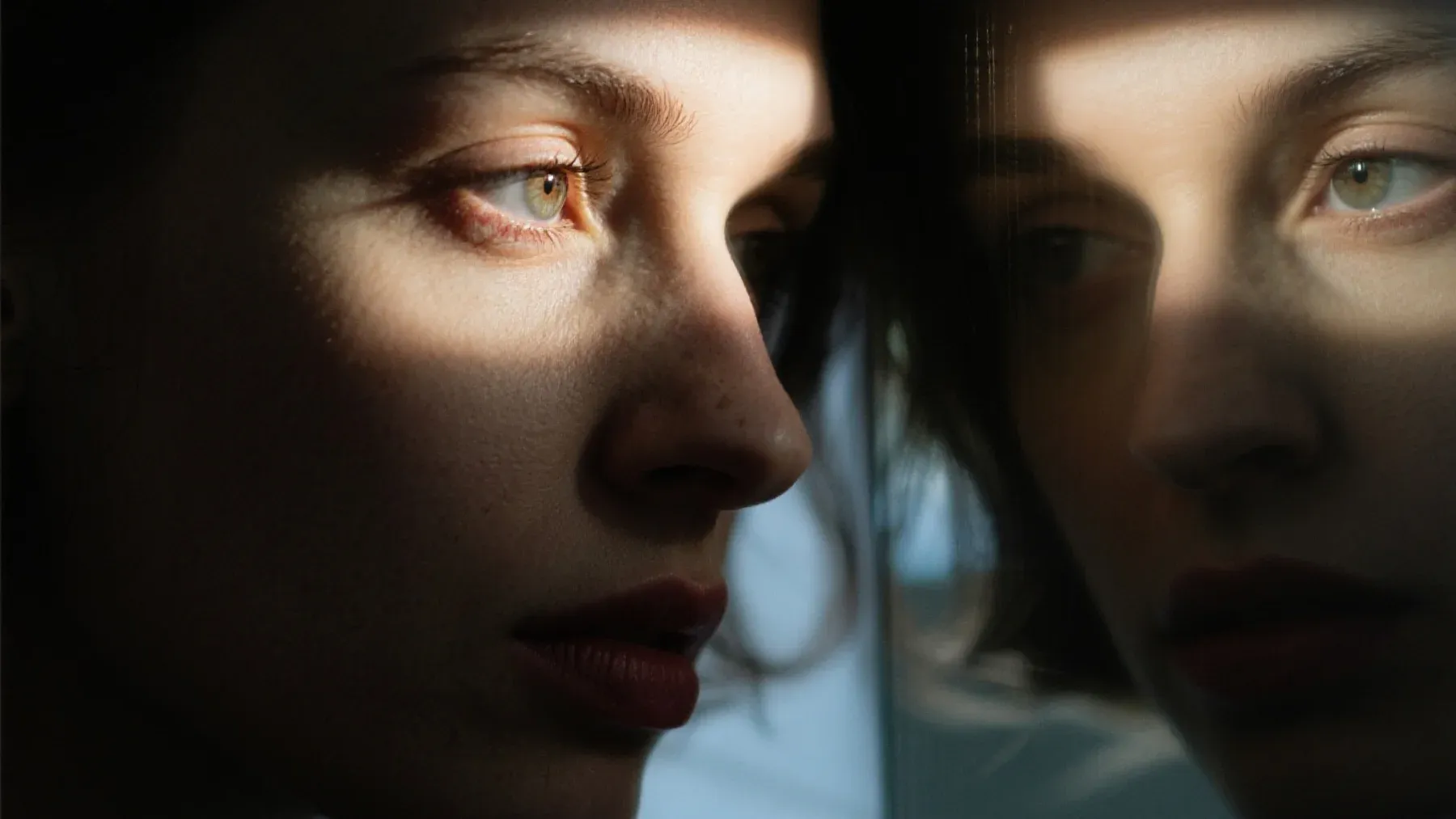 A person studies a reflection while their surroundings remain indistinct, representing the difference between recognizing oneself and accessing a missing period of life.