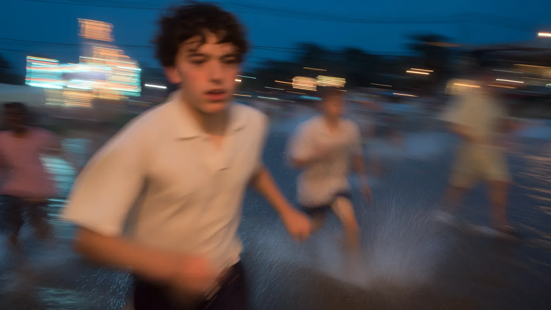 Several figures running across a wet urban space capture the uncertainty and changing distance that drive a pursuit.