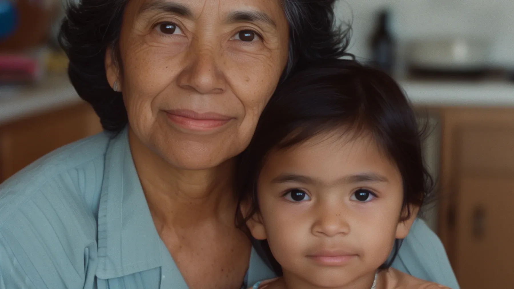 A grandmother and child share a quiet kitchen moment, showing how language can be learned through relationship, routine, and generational memory.