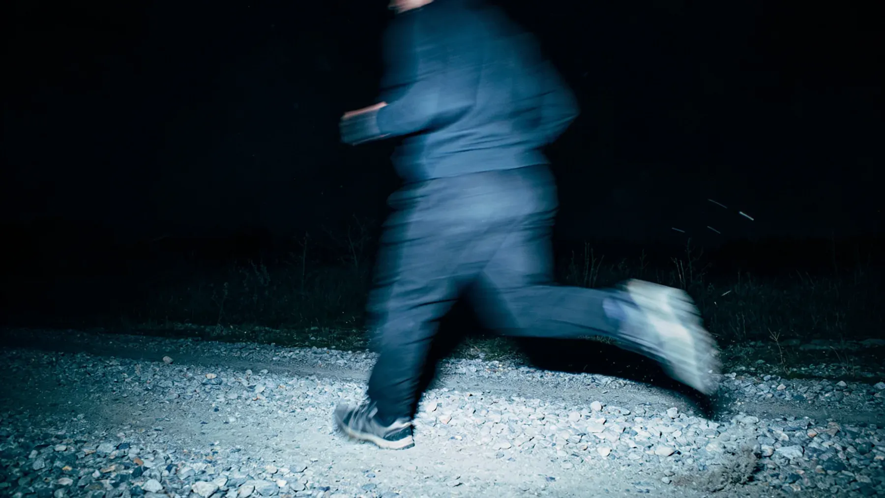 A runner crosses rough ground at night, showing that leaving containment begins a different physical and moral problem rather than ending the story's pressure.