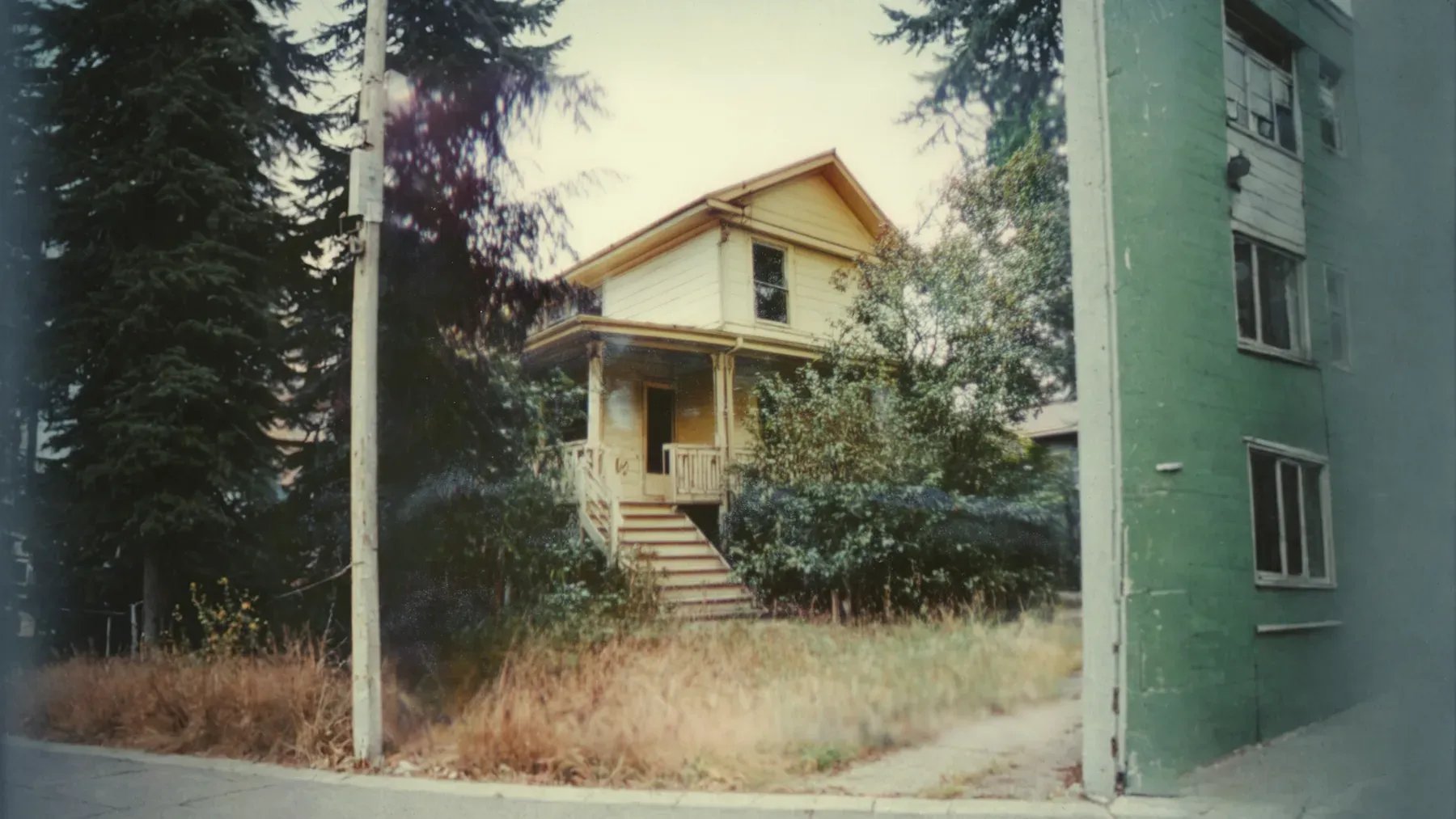 An aging house stands between newer buildings, showing how one inheritance can accumulate value, neglect, and neighborhood pressure at the same time.