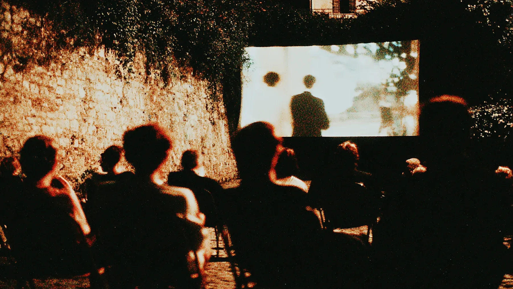 A neighborhood audience watches a film outdoors at night, turning the group's private work into a future that includes the wider community.