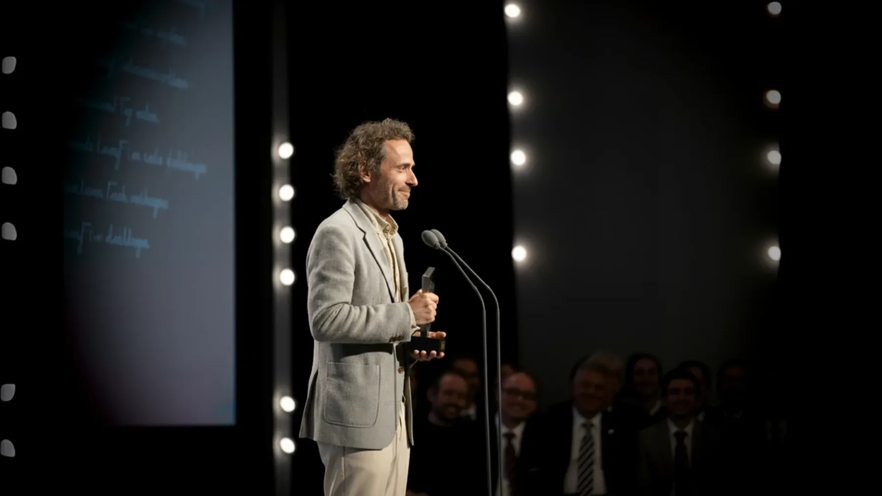 A person addressing an award ceremony, representing the conflict between an institution's public story and a character's private moral account.