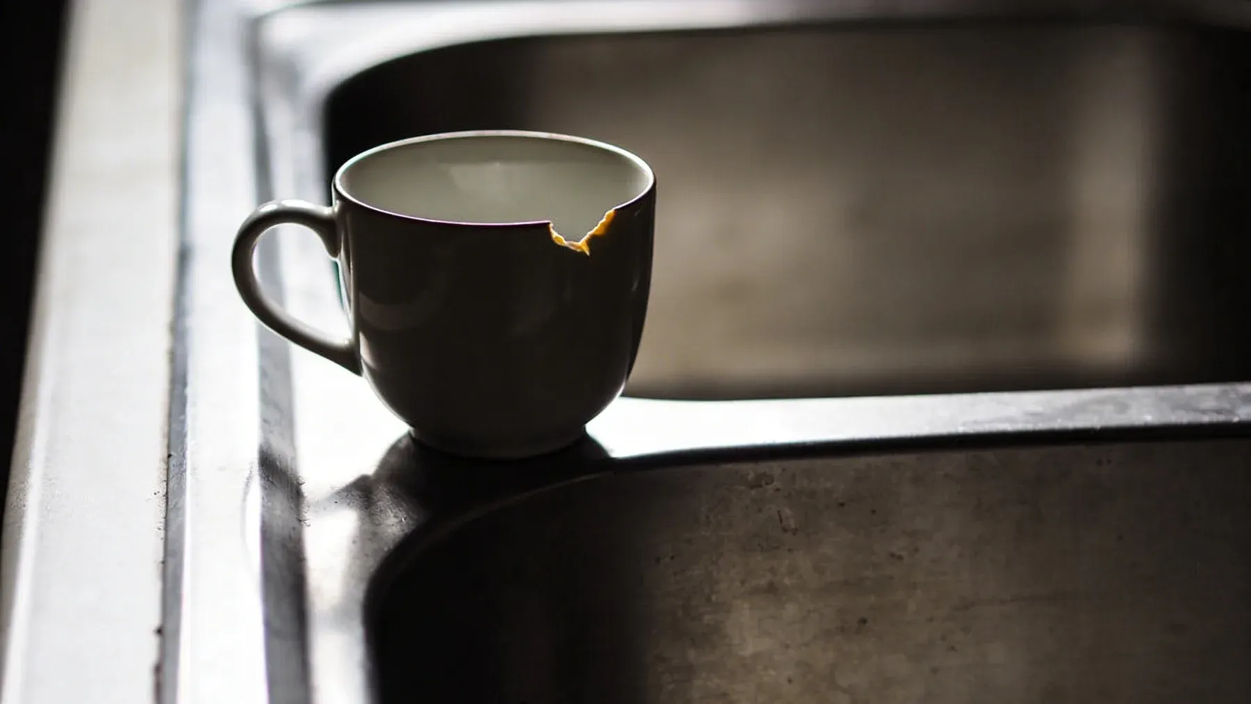A chipped cup left beside a sink, where changed condition and placement can carry the aftermath of a relationship scene.