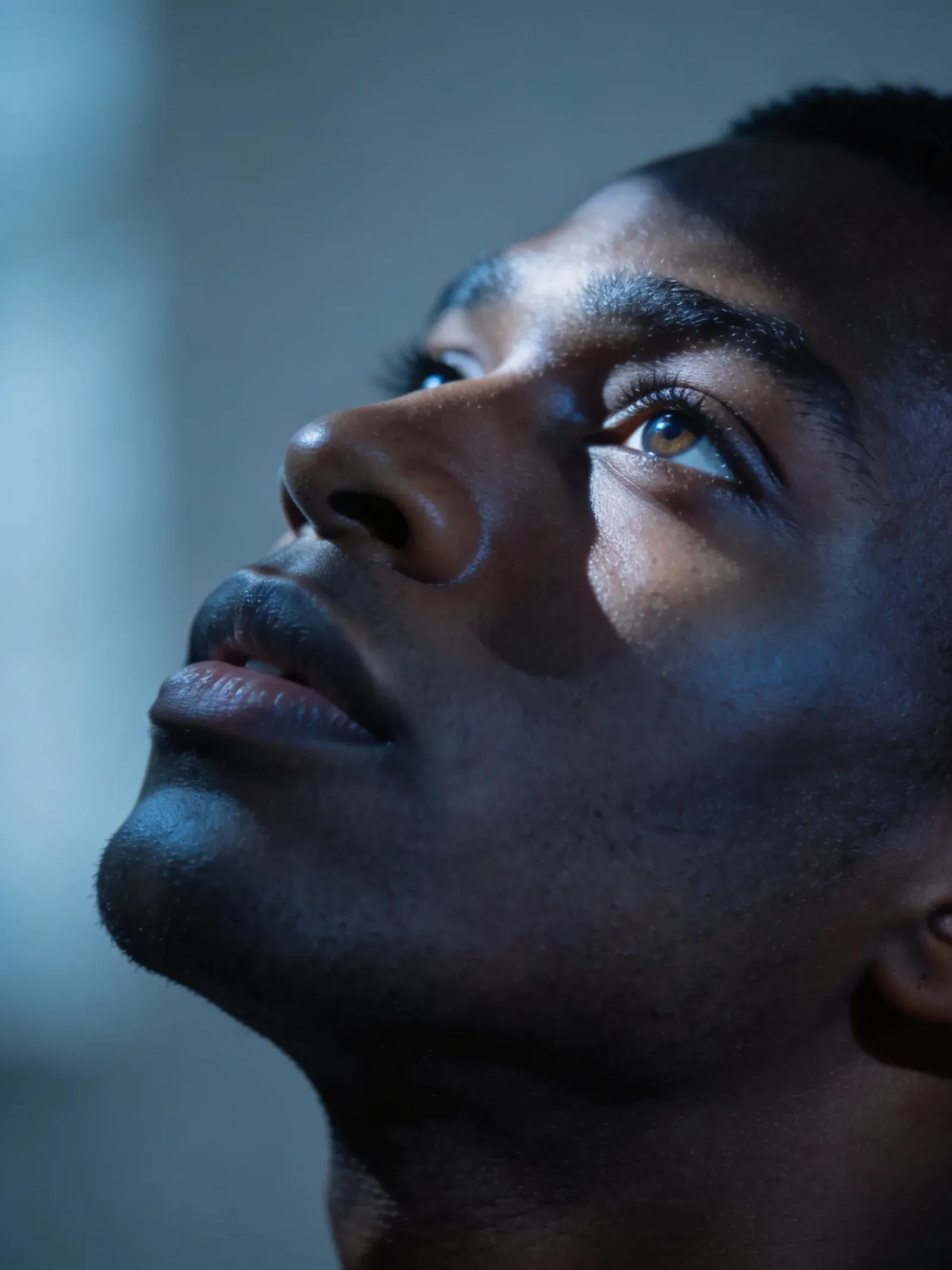 A close-up portrait of a thoughtful man looking upward in cool blue light.