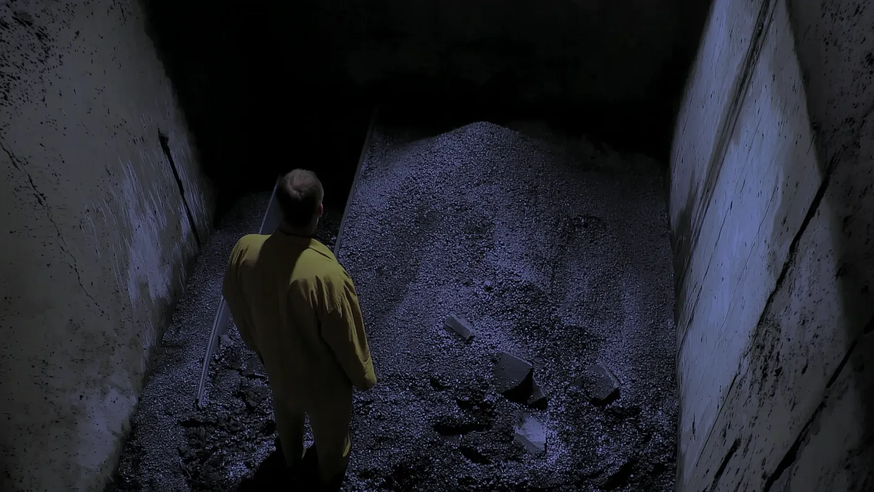 A worker stands alone inside a narrow industrial passage, making distance, access, and limited visibility concrete rather than abstract.