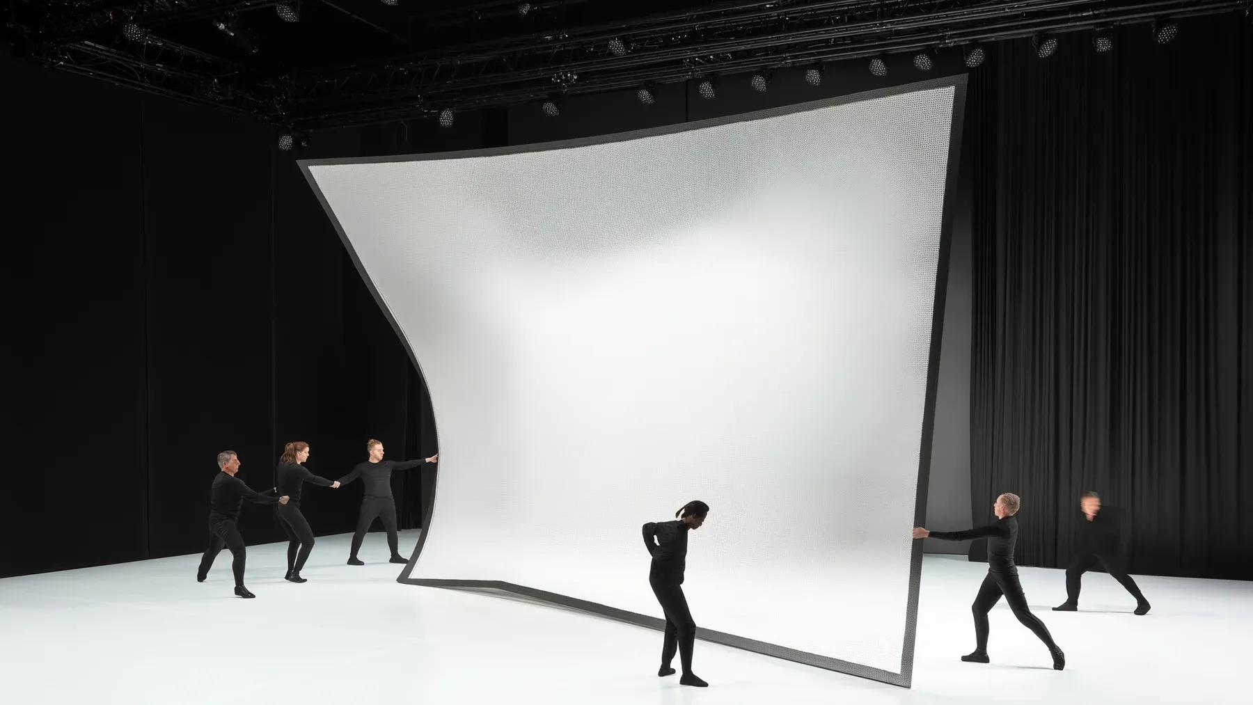A stage crew moves a large scenic panel beneath a lighting rig, showing how each technical choice changes the routes available to the next beat.
