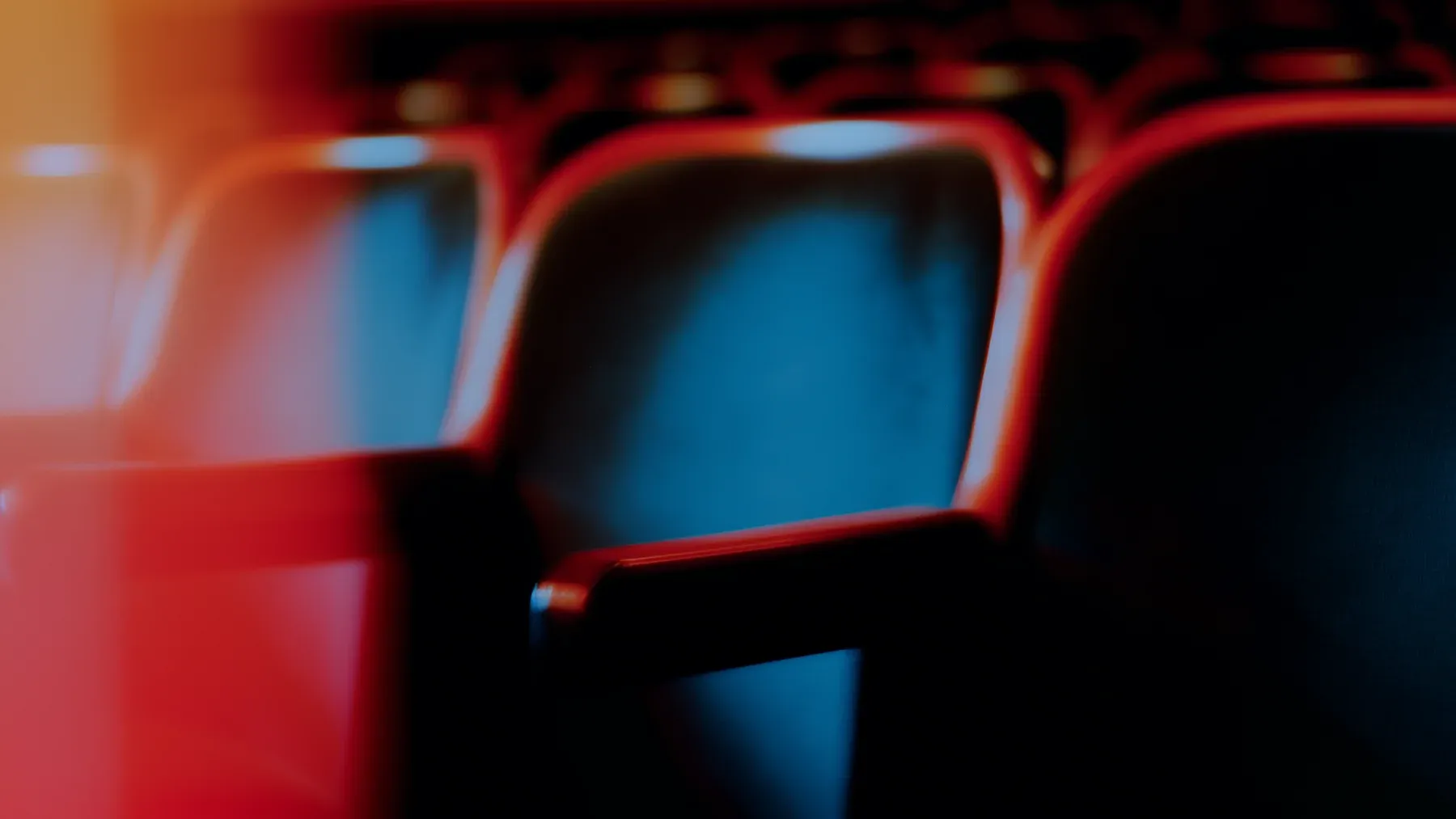 Rows of empty theater seats under red and blue light make the closed balcony a visible consequence that the following scene must inherit.