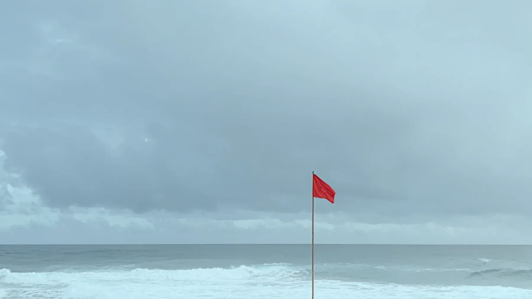 A red warning flag beside a stormy shoreline, representing the kind of clear signal an exhausted character can still misread or fail to connect with a changing record.