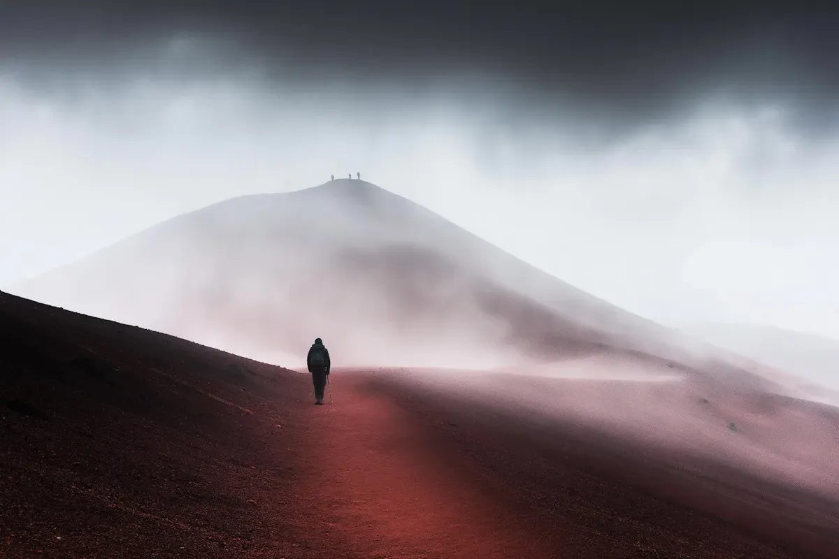 A lone traveler moving through red earth and fog, echoing the threshold-crossing energy of transformational stories.